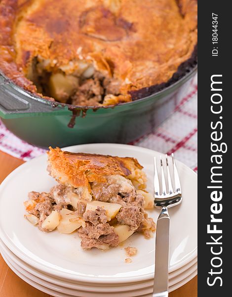 Pot pie with beef, veal and pork meat in a green oven cookware. Portion in a white plate.Very shallow depth of field. Pot pie with beef, veal and pork meat in a green oven cookware. Portion in a white plate.Very shallow depth of field.