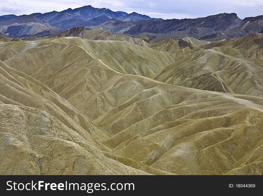 Long view of eroded, hilly landscape with no vegitation and jagged, rocky mountains in the background in Death Valley, CA. Long view of eroded, hilly landscape with no vegitation and jagged, rocky mountains in the background in Death Valley, CA.