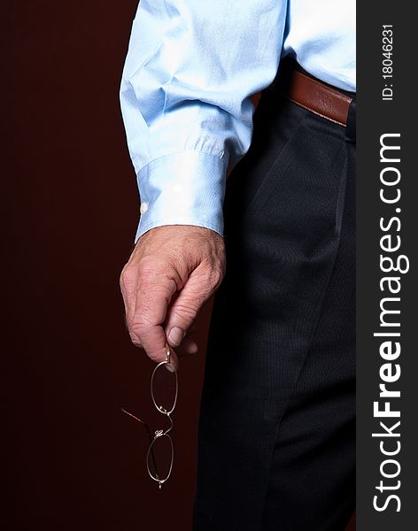 The arm and sleeve of a business man holding glasses against a solid color background in a vertical orientation