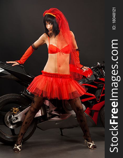 Beautiful dark-haired girl in a red wedding dress on motorbike isolated on black background in studio. Beautiful dark-haired girl in a red wedding dress on motorbike isolated on black background in studio