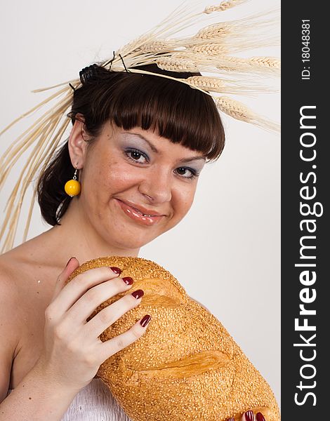 Beautiful brunette girl with ears of wheat in her hair is eating a bread isolated on the white background. Beautiful brunette girl with ears of wheat in her hair is eating a bread isolated on the white background