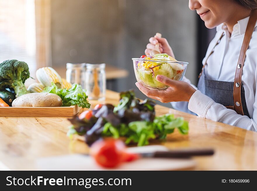 Closeup image of a beautiful female chef cooking and holding a bowl of fresh mixed vegetables salad to eat in kitchen