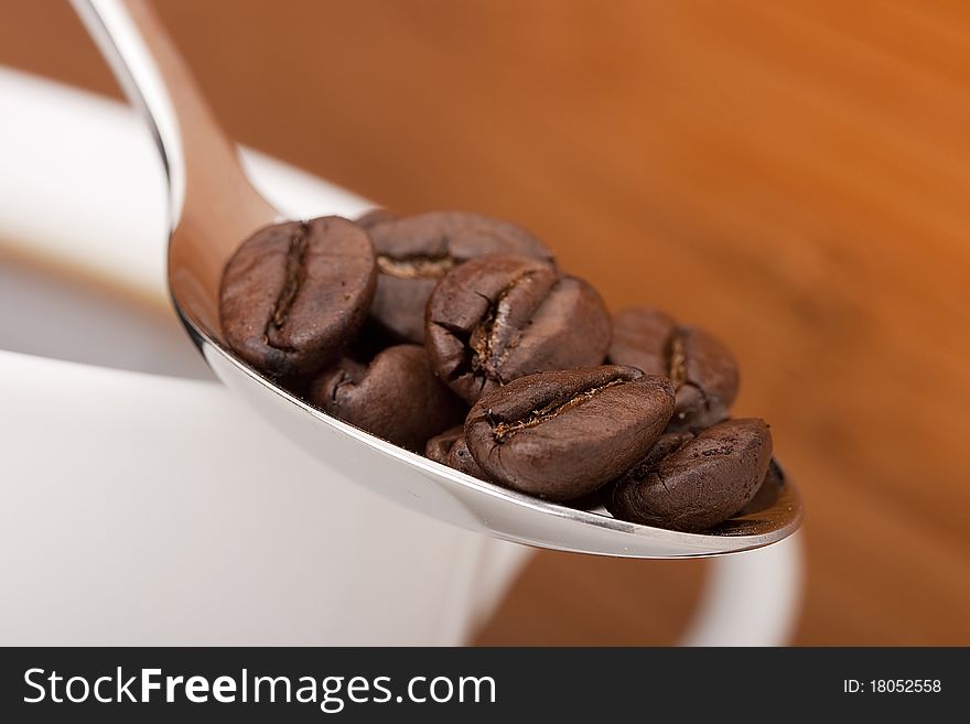 Coffee beans in a teaspoon, close up, not the focus of a cup with a coffee drink.
