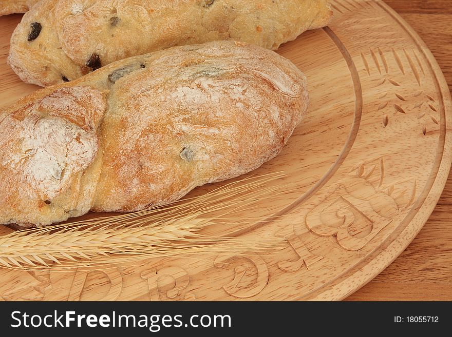 Olive bread on a carved beech wood board with wheat.