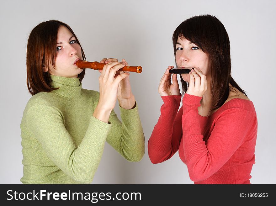 Two brunette girls in bright shirts playing on flute and harp, looking at camera. Two brunette girls in bright shirts playing on flute and harp, looking at camera