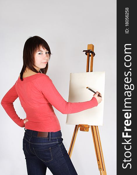 Young girl in red shirt standing near easel, painting and looking back. Young girl in red shirt standing near easel, painting and looking back