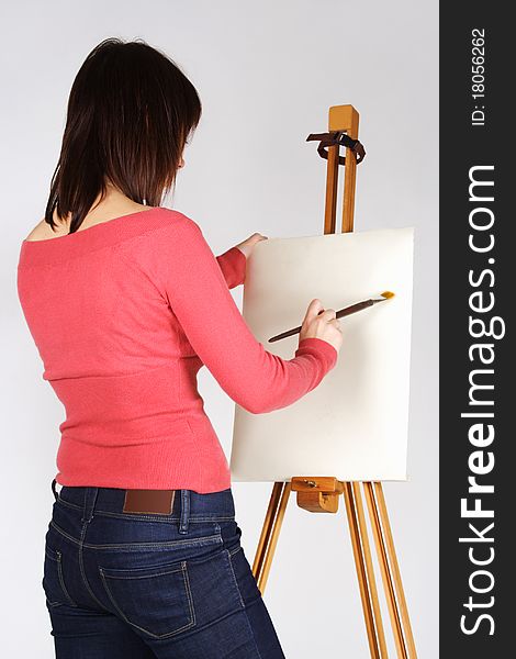 Young girl in red shirt standing near easel and painting, back view. Young girl in red shirt standing near easel and painting, back view