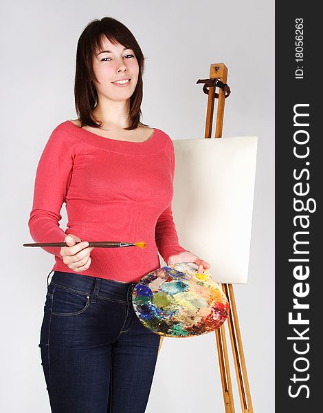 Young girl in red shirt standing near easel, holding brush and palette, smiling. Young girl in red shirt standing near easel, holding brush and palette, smiling