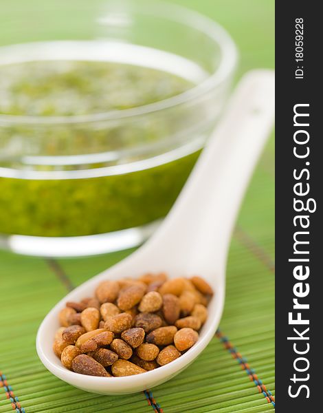 Pine nuts in a spoon with pesto sauce in the background. Extreme shallow depth of field.