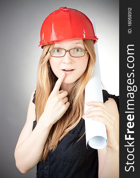 Young woman in helmet with blueprint, with grey background. Young woman in helmet with blueprint, with grey background