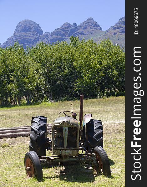 An old farm tractor on a scenic yard with trees and blue mountains