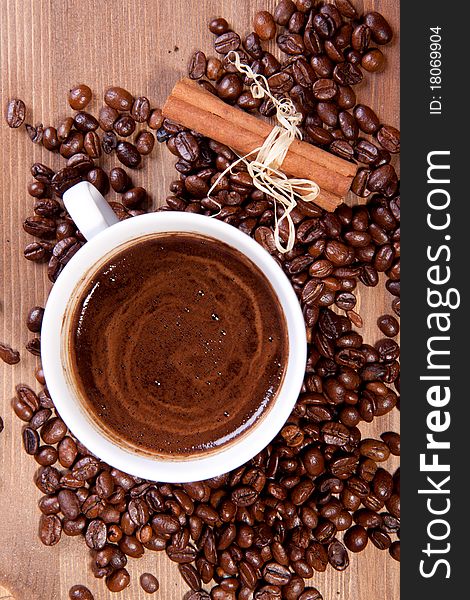 Cup of black coffee and fragrant fried coffee beans and cinnamon on a wooden table. Cup of black coffee and fragrant fried coffee beans and cinnamon on a wooden table