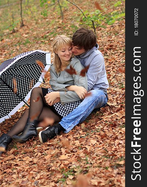 Young cheerful smiling couple sitting on the ground in the park. Young cheerful smiling couple sitting on the ground in the park