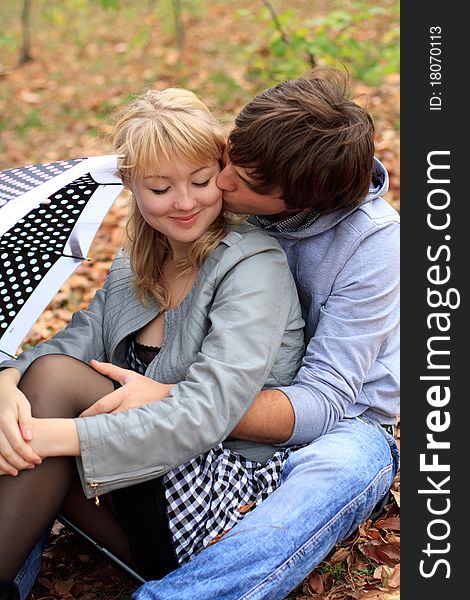 Young cheerful smiling couple sitting on the ground in the park. Young cheerful smiling couple sitting on the ground in the park