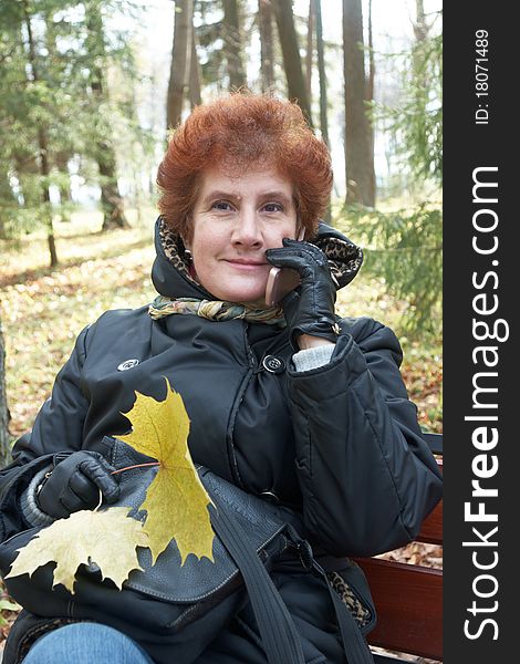 Senior lady portrait sitting on a bench and talking on cell phone in autumn park. Senior lady portrait sitting on a bench and talking on cell phone in autumn park