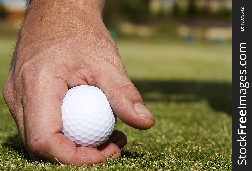 A close up of a man's hand placing a golf ball on a tee. A close up of a man's hand placing a golf ball on a tee