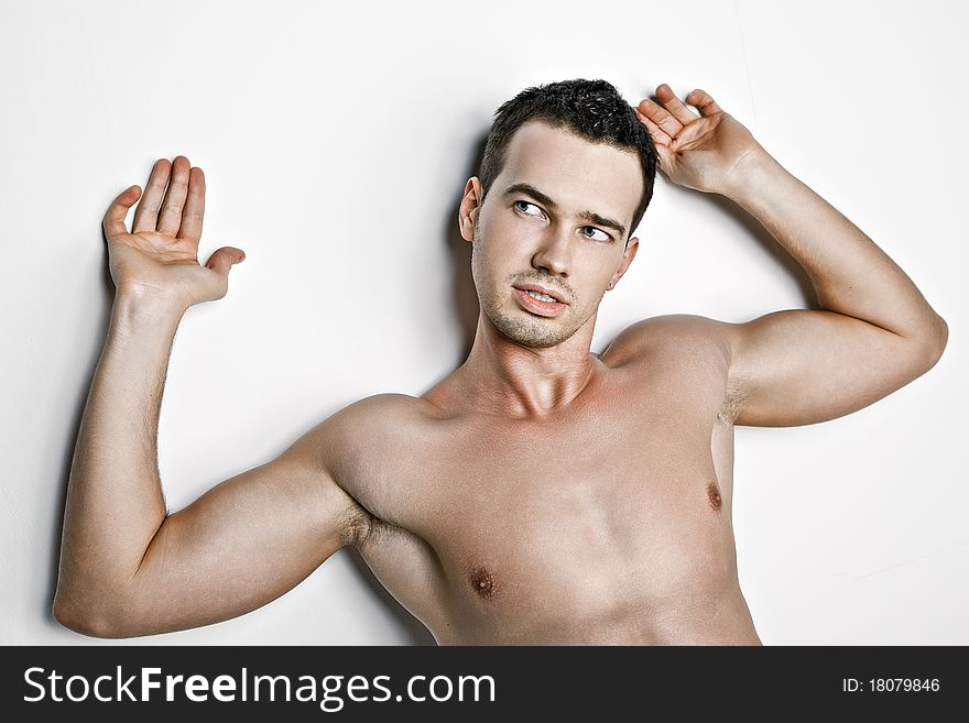A guy with a naked torso at white background with hands up