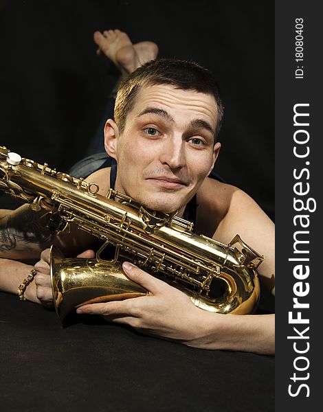 The young jazzman lie on the floor with saxophone