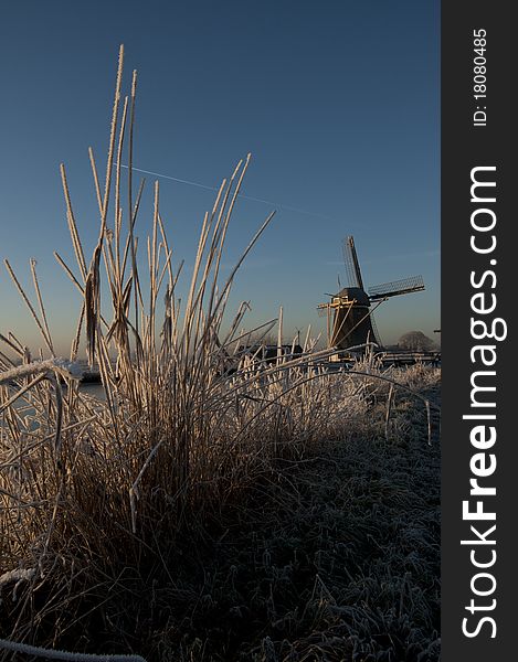 A frozen riverbank with an old Dutch windmill in the background. A frozen riverbank with an old Dutch windmill in the background.