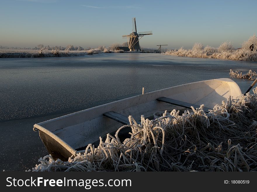 A Dutch landscape of a frozen river with an rowboat and old windmill. A Dutch landscape of a frozen river with an rowboat and old windmill.