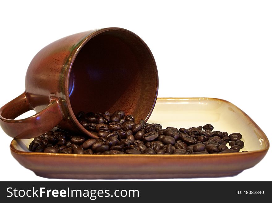 Coffee beans spilling into dish from cup - isolated against white. Coffee beans spilling into dish from cup - isolated against white