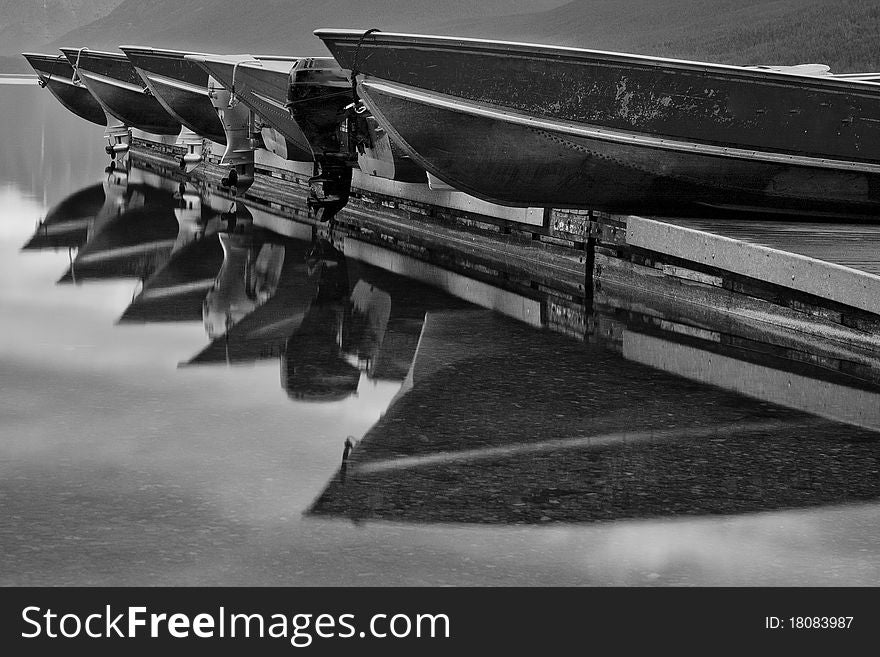 Black and white photograph of boats resting on the dock at Apgar reflecting in a calm Lake McDonald. Glacier National Park, Montana. Black and white photograph of boats resting on the dock at Apgar reflecting in a calm Lake McDonald. Glacier National Park, Montana