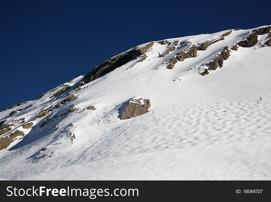 A view on alpine ski slope with skiers far away. A view on alpine ski slope with skiers far away