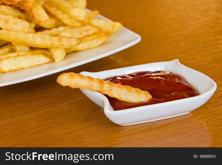 Close-up of a single french fry in bowl of ketchup, plate with fries in the background. Close-up of a single french fry in bowl of ketchup, plate with fries in the background