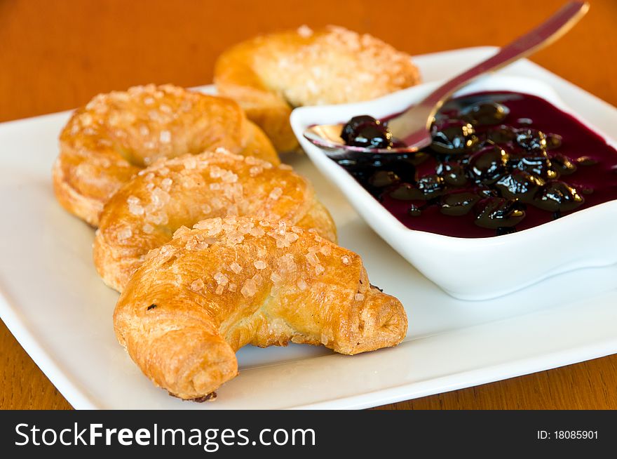 White plate of freshly baked, golden croissants with a bowl of blackberry jelly and a spoon. White plate of freshly baked, golden croissants with a bowl of blackberry jelly and a spoon