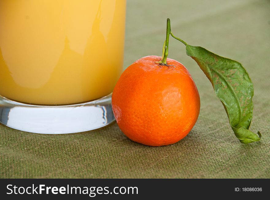 Close-up of a single orange fruit with a glass of orange juice on green napkin. Close-up of a single orange fruit with a glass of orange juice on green napkin