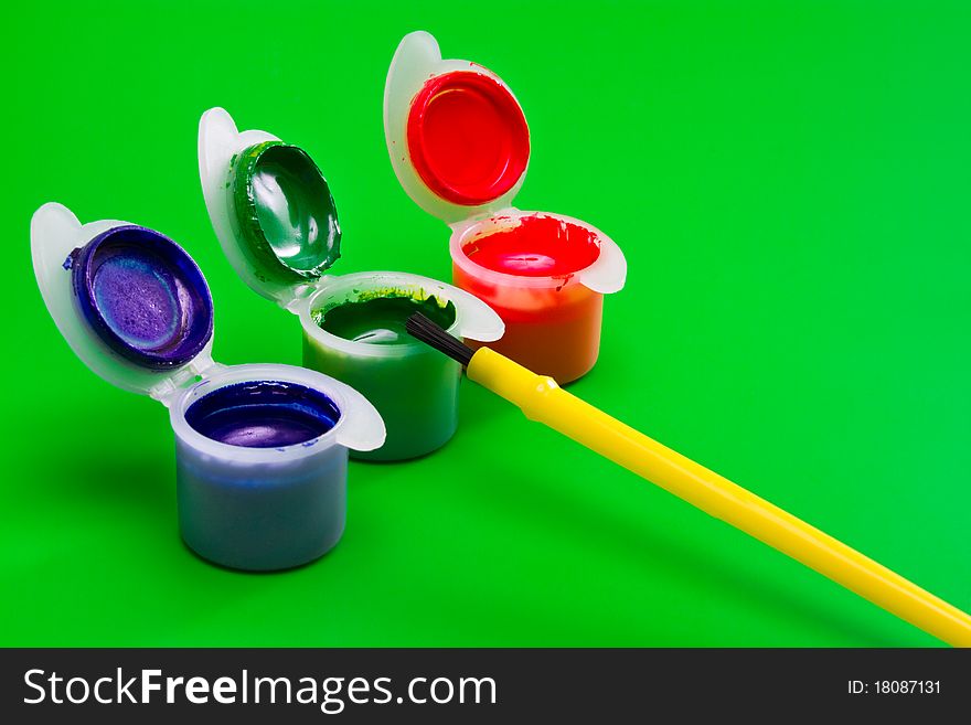 Three cans of paint: green, red, blue with paintbrush on green background. Three cans of paint: green, red, blue with paintbrush on green background