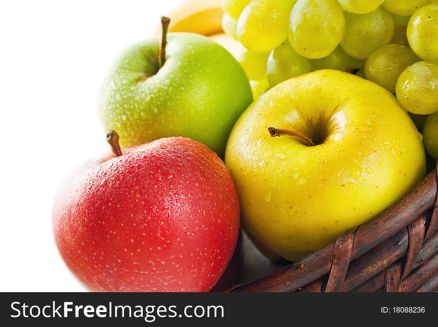 Three apples in different colors placed in a wicker basket with some grape and banana isolated on white. Three apples in different colors placed in a wicker basket with some grape and banana isolated on white