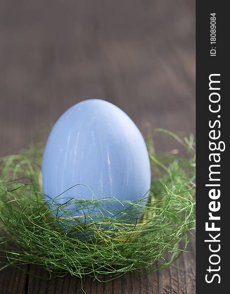 Blue easter egg in nest on wooden background
