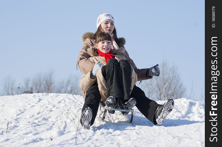 Two happy sisters sledding at winter time