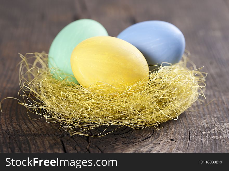 Colorful easter eggs in nest on wooden background