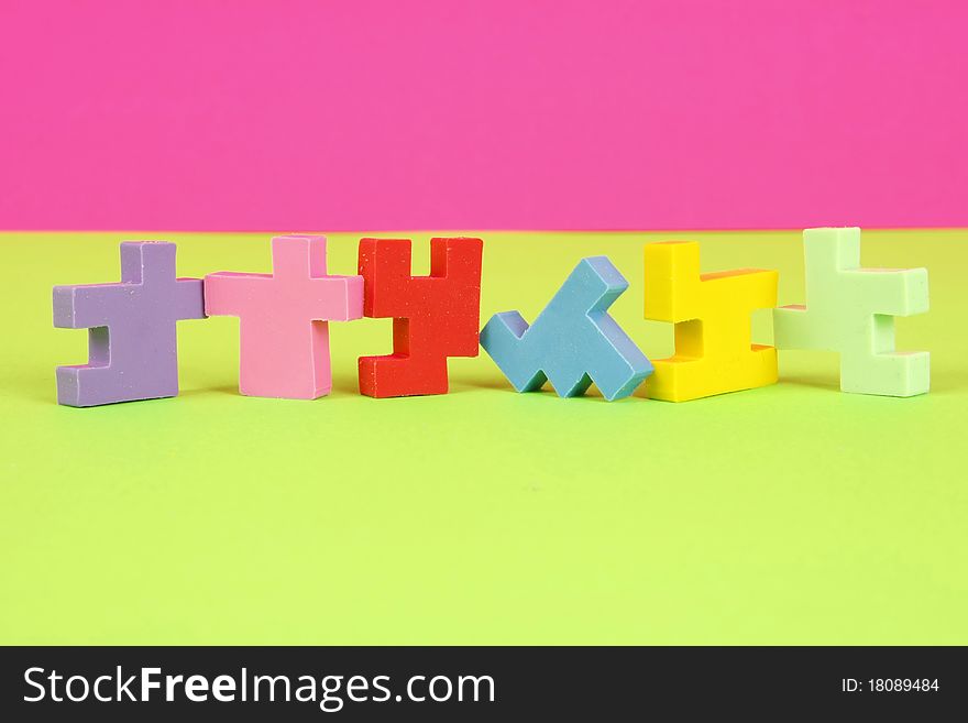 Bright colored puzzle piece erasers in a row with a pink and green background. Bright colored puzzle piece erasers in a row with a pink and green background.