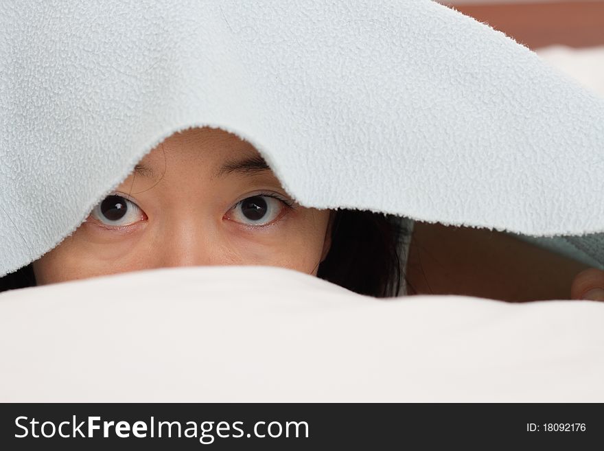 An Asian woman in bed peeking from under a blanket