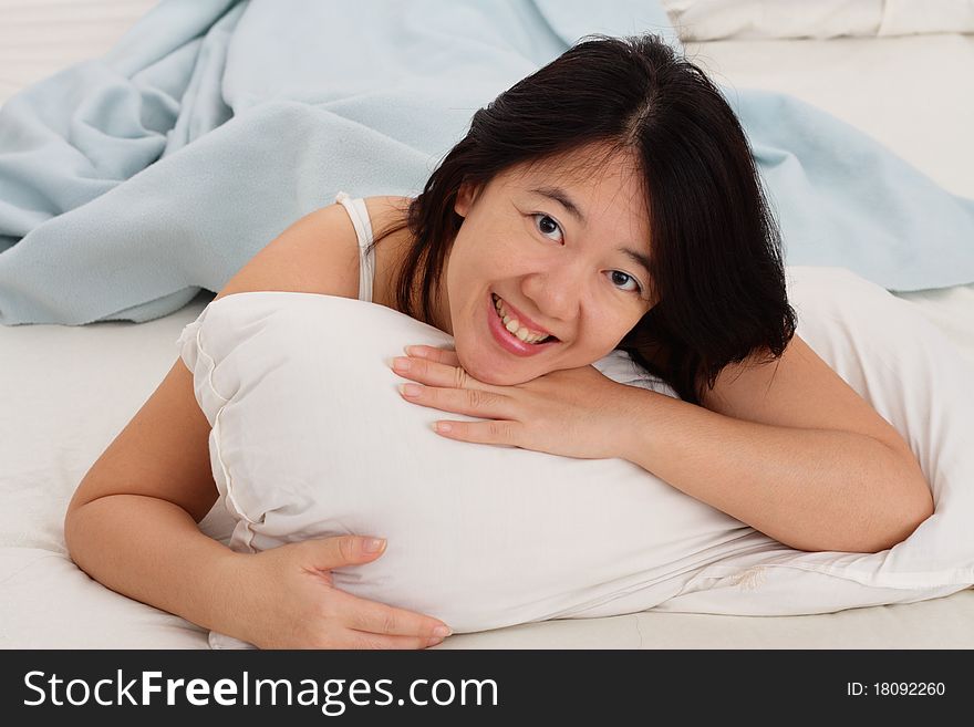 A smiling Asian woman hugging a pillow in bed looking at photographer. A smiling Asian woman hugging a pillow in bed looking at photographer
