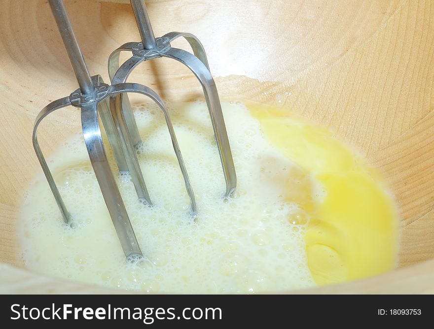 Beating eggs with an electric mixer in a wooden bowl. Beating eggs with an electric mixer in a wooden bowl