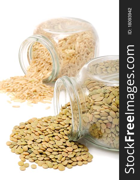 Glass jars with lentils and brown rice on a white background