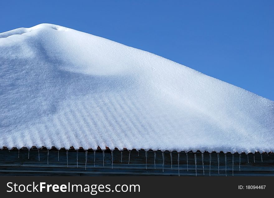 Roof of the house with icicles on a background of the blue sky. Roof of the house with icicles on a background of the blue sky