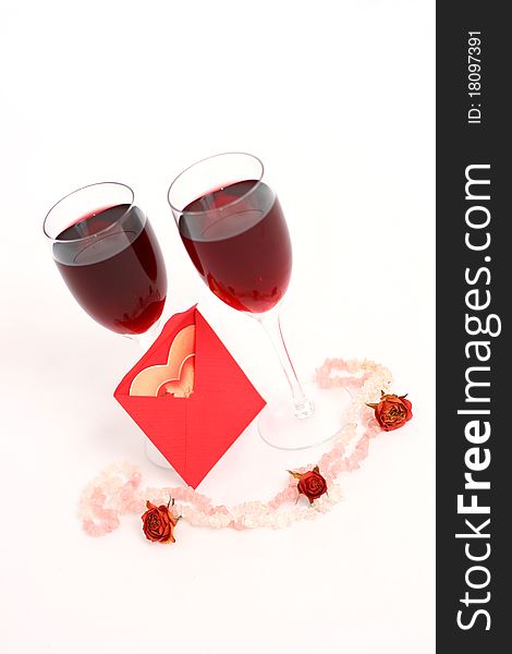 Two red wine glasses and a heart-shaped postcard in a red envelope. Two red wine glasses and a heart-shaped postcard in a red envelope