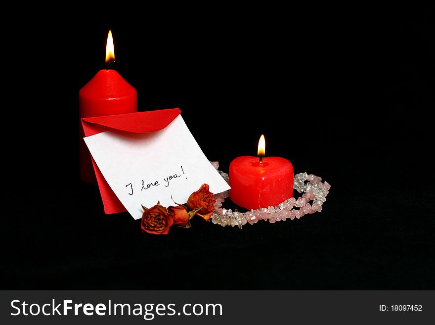 Love message handwritten on a white card with red envelope and burning red candles isolated on black. Love message handwritten on a white card with red envelope and burning red candles isolated on black