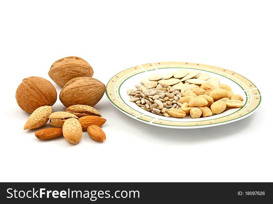 Mix of dry fruits (walnuts, almonds, peanuts) and a plate of seeds (sunflower and pumpkin seeds) isolated on white. Mix of dry fruits (walnuts, almonds, peanuts) and a plate of seeds (sunflower and pumpkin seeds) isolated on white