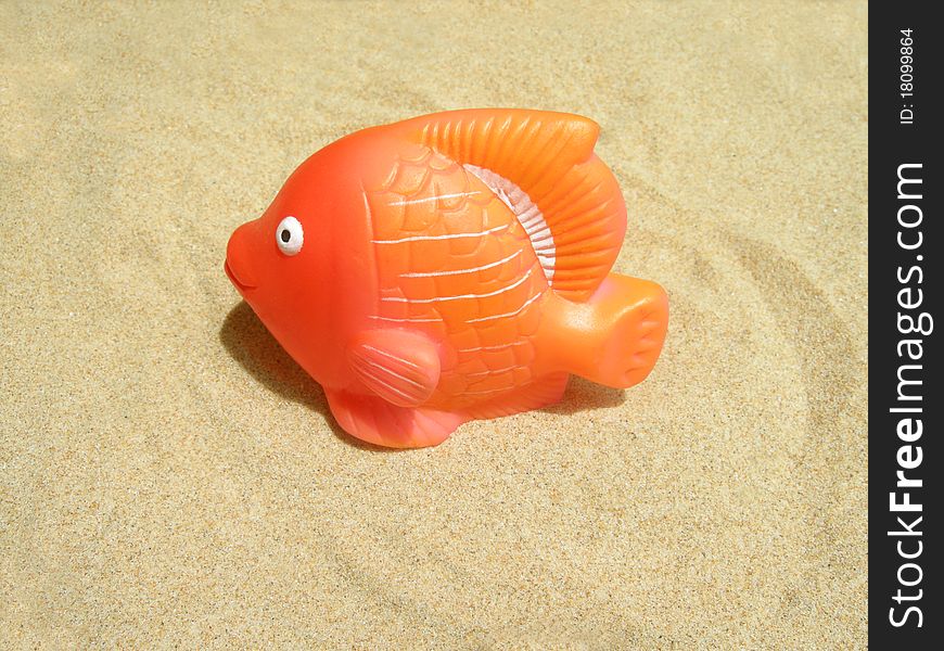 Orange-colored plastic fish in the sand.