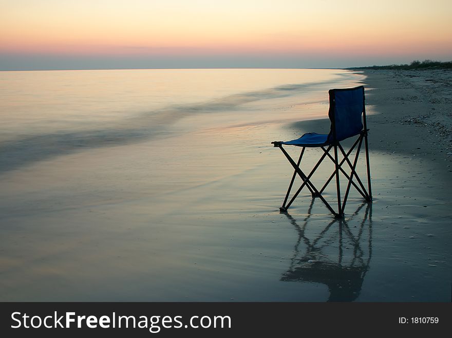 Chair standing on a sand on a seaside with a sunset on a horizon. Chair standing on a sand on a seaside with a sunset on a horizon