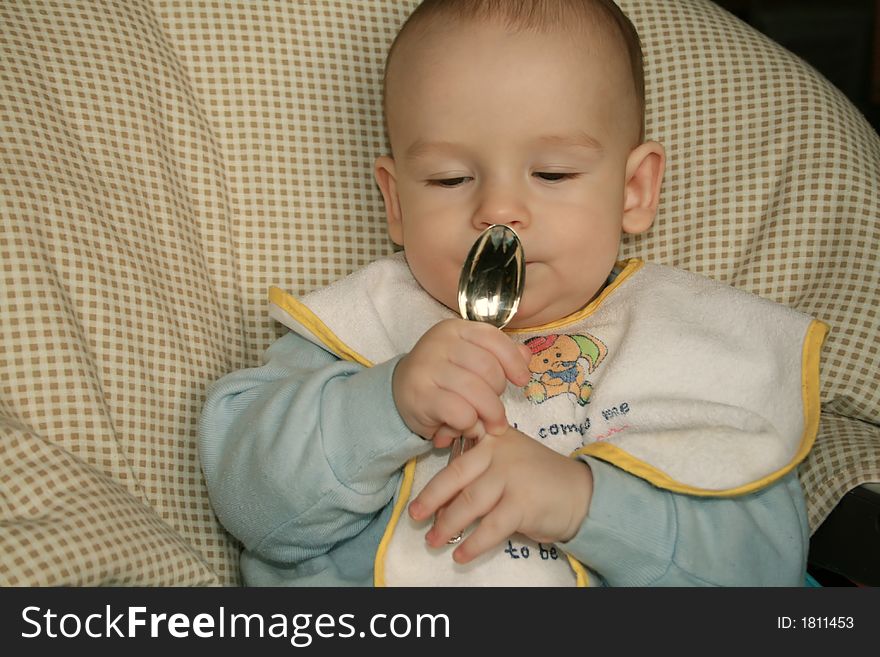 The kid of 6 months sits with the spoon. The kid of 6 months sits with the spoon