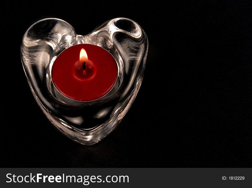 Valentines heart in glass  with candle isolated one a black background. Valentines heart in glass  with candle isolated one a black background
