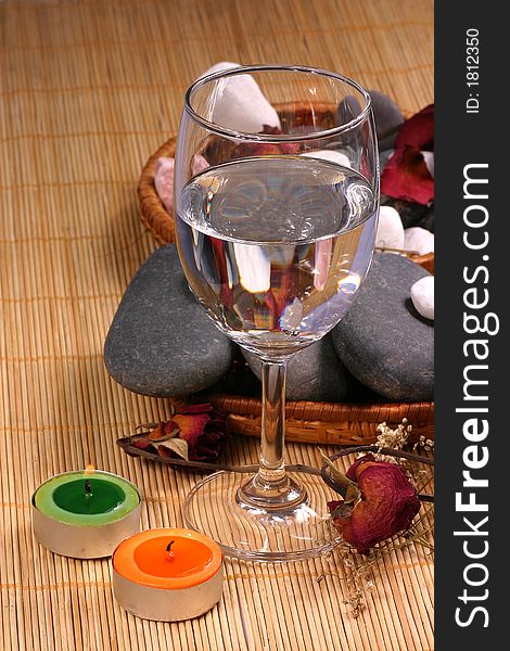 A romance view of a glass, natural pebbles and dried rose petals on the rattan background. Suitable for spa, relaxation and romance setting. A romance view of a glass, natural pebbles and dried rose petals on the rattan background. Suitable for spa, relaxation and romance setting.
