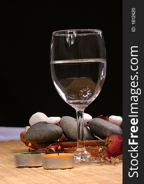 A romance view of a glass, natural pebbles and dried rose petals on the rattan background. Suitable for spa, relaxation and romance setting. A romance view of a glass, natural pebbles and dried rose petals on the rattan background. Suitable for spa, relaxation and romance setting.